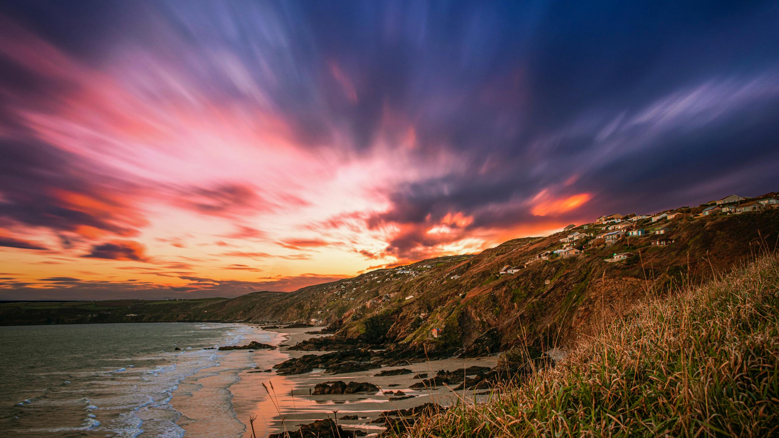 Stunning sunset over a rugged coastline with vibrant clouds and serene sea.